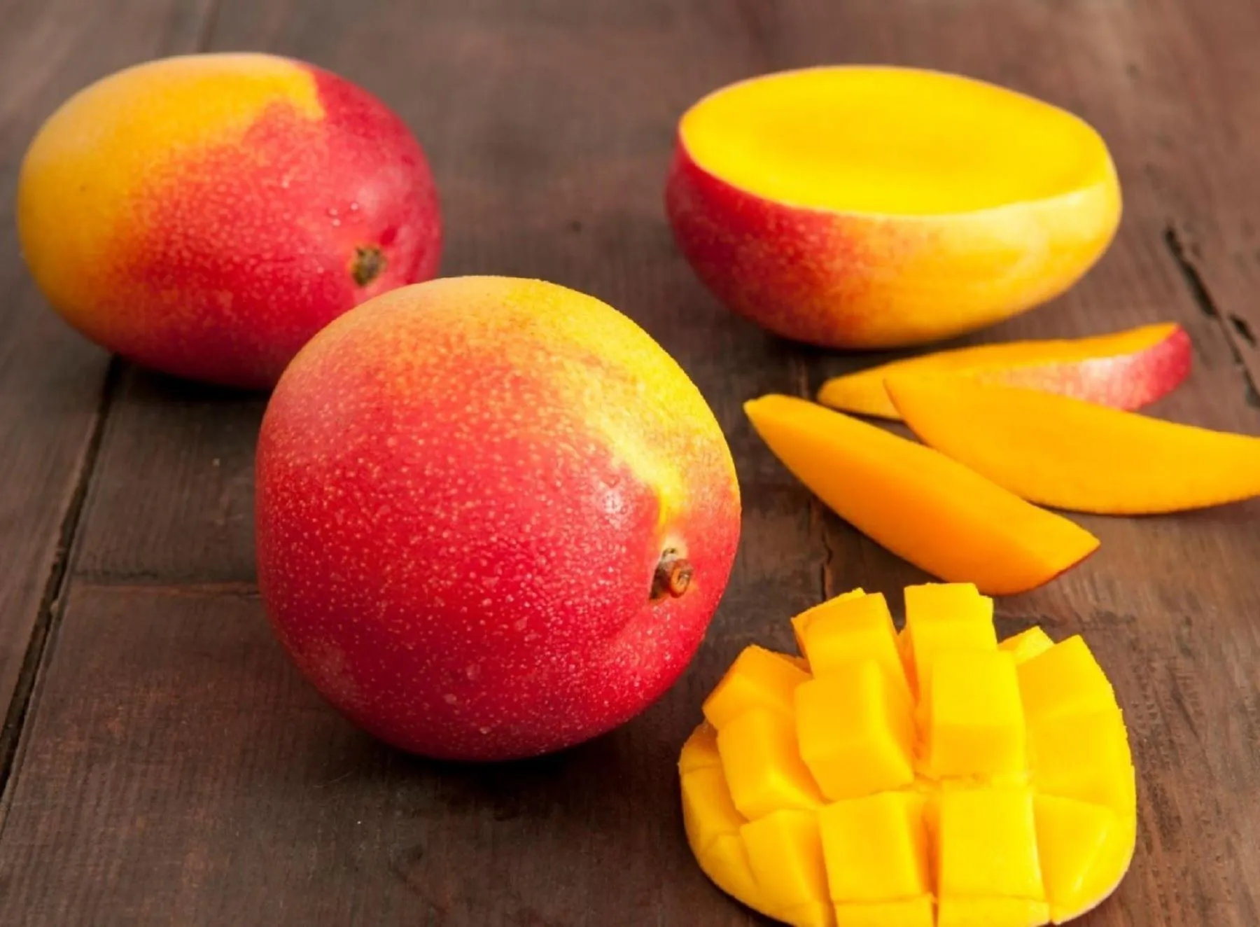 Mangos Kent enteros y en tajadas sobre madera oscura